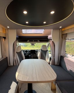 Blick von der Sitzgruppe über den Tisch
                           zum Fahrerhaus und zum Hubbett des Chausson Titanium 640.