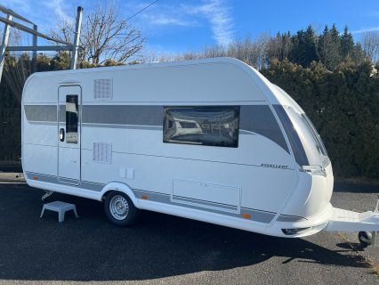 Weißer
                           Hobby Excellent 460 SL mit grauem Seitenstreifen in schräger Seitenansicht auf einem asphaltierten Platz. Sichtbar sind Eingangstür,
                           großes Seitenfenster, Lüftungsgitter, Rad, Deichsel und die abgerundete Frontpartie.