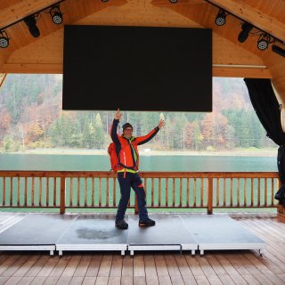 Person in Wanderkleidung steht auf einer überdachten Bühne mit Blick
                           über den Pillersee.