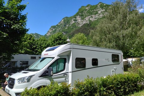 Wohnmobil am Stellplatz mit viel Grünn und Bergen im Hintergrund.