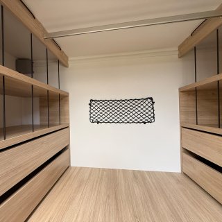 Blick in den Kleiderschrank im Heck mit offenen Ablagefächern,
                           Schubladen und einem Gepäcknetz.