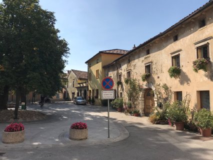 Auf dem
                           Bild sieht man eine Straße in Vipava, Slowenien. Auf der rechten Seite ist ein charmantes, blumenbedecktes Haus, welche typisch
                           für die historische Architektur der Region ist.