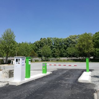 Einfahrt von CAMPING-CAR PARK mit Schranken und Bäumen im Hintergrund.