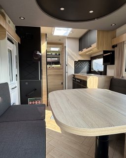 Wohnbereich des Chausson Titanium
                           640 mit großer Tischplatte, gegenüberliegenden Sitzbänken und Küchenzeile im Hintergrund.