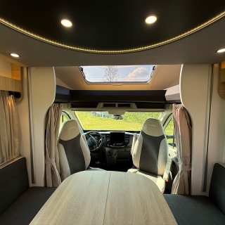 Blick vom Wohnraum über den Tisch und
                           die Sitzgruppe zum offenen Fahrerhaus des Chausson Titanium 640.