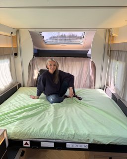 Person sitzt auf dem abgesenkten Hubbett im hellen
                           Innenraum des Chausson Titanium 640.