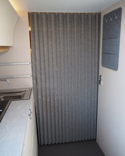 Graue Trennwand in der Mitte des Ganges im Wohnwagen
                           Adria Adora 593 UP mit Kleiderhaken rechts und Küche/Waschbecken links davon.