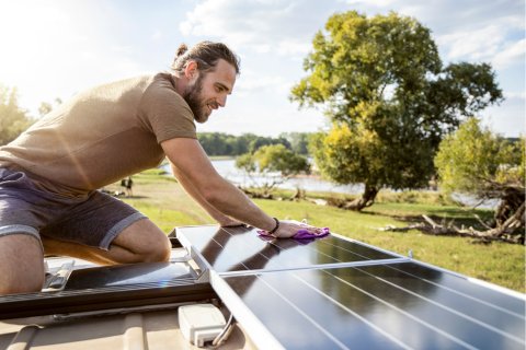 Ein Mann montiert ein Solarpanel auf dem Dach eines Wohnmobils.