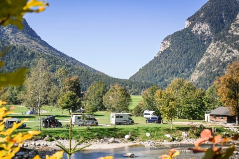 Campingbusse am Fluss vor Bergpanorama in herbstlicher Stimmung