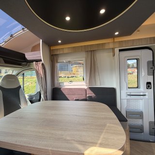 Sitzgruppe des Chausson Titanium 640 mit großem
                           Tisch, seitlichem Fenster und Aufbautür im Wohnbereich.