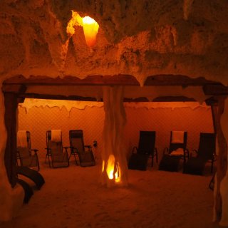 Orange beleuchtete Salzgrotte mit
                           mehreren Liegestühlen, Holzbalken und einer beleuchteten Säule.