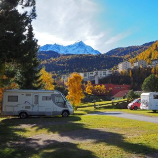 Mit Wohnmobilen und Van belegte Parzellen auf dem Campingplatz Camping Sölden im Herbst mit Bergpanorama
                           im Hintergrund.