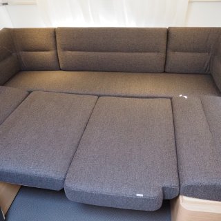 Sitzfläche/dunkelgraue Polster zu Schlafplätzen umgebaut in Inneren eines Wohnwagens.
