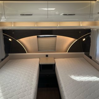 Schlafbereich im Hobby Excellent 460 SL mit
                           zwei getrennten Betten, hellen Matratzen, mittigem Ablagetisch und Oberschränken. An der Stirnseite befinden sich ein Fenster
                           mit Rollo, indirekte Beleuchtung und zwei Leselampen.