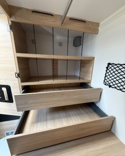 Geöffneter Schrank im Heck des Chausson
                           Titanium 640 mit zwei ausgezogenen Schubladen, offenen Ablagefächern und elastischen Haltebändern.