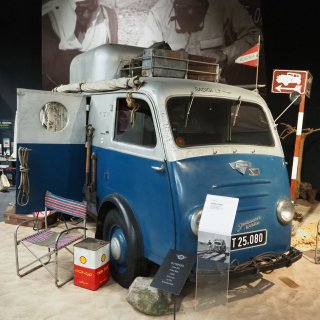 Historisches blau-weißes Expeditionsfahrzeug mit
                           Dachgepäck, Reiseausrüstung und Österreich-Fähnchen im Motorradmuseum.