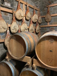 Auf dem Bild sind einige Weinfässer in einem Weinkeller zu sehen. An
                           der Wand dahinter hängen zudem einige Schinkenbeine.