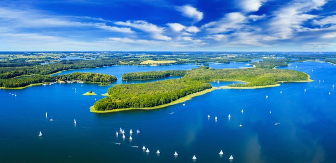 Luftaufnahme von Masuren, viele kleine grüne Inseln inmitten dunkelblauer Seen, viele Segel- und
                           Ausflugsboote tummeln sich am Wasser.