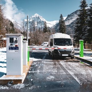 Wohnmobil hinter Schranken im Winter bei einer Einfahrt von CAMPING-CAR PARK mit Bergpanorama im HIntergrund.