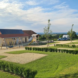 Spielplatz mit
                           Holzgerüst, gelber Rutsche, mehreren Schaukeln und Sandfläche auf der begrünten Campinganlage.