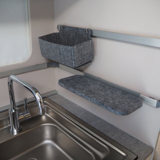 Waschbecken in der Küche des Wohnwagens Adria Adora
                           593 UP mit Aluschienen an der Wand, in welche eine kleine graue Ablagebox eingehängt ist.