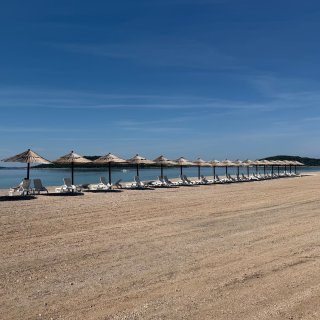 Strandbereich des Camping Resort Šibenik
                           mit Liegen und Sonnenschirmen direkt am Meer. Im Hintergrund sind die Küste und vorgelagerte Inseln zu sehen.