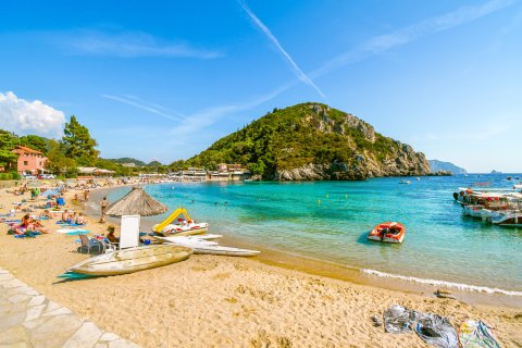 Ein sonniger Tag am Strand von Palaiokastritsa, während Touristen sich
                           sonnen und im Meer schwimmen, auf der Insel Korfu, Griechenland.