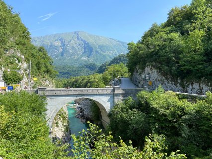 Das Bild zeigt die Napoleonbrücke über den Fluss Soča bei Kobarid
                           in Slowenien. Im HIntergrund sieht man Wälder und einen Berg.
