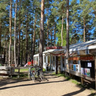 Der Kinderclub
                           im familienfreundlichen Camping Resort Havelberge. Vor dem hellen Gebäude unter hohen Kiefern stehen Fahrräder, im Hintergrund
                           ist der angrenzende Waldseilgarten erkennbar.