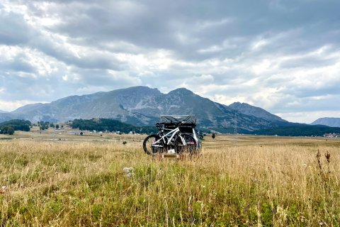 Auto mit Dachzelt in eine Wiese mit Bergen im Hintergrund.