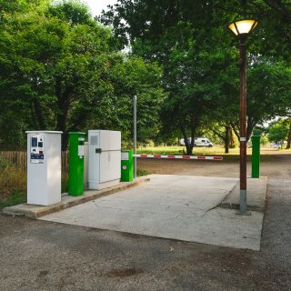 Einfahrt von CAMPING-CAR PARK mit Schranken mit Bäumen und einigen Wohnmobilen, welche auf Plätzen stehen,
                           im Hintergrund.
