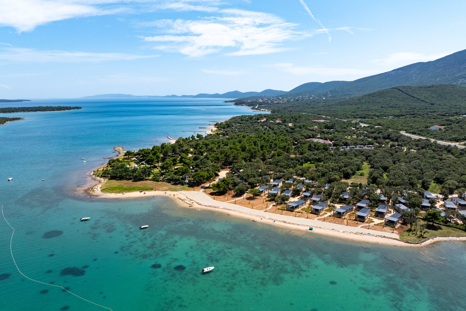 Luftaufnahme des unter
                                 der Baumkrone bedeckten Campingplatzes am Strand mit kristallklarem grün-blauem Wasser und mit Mobilheimen 
