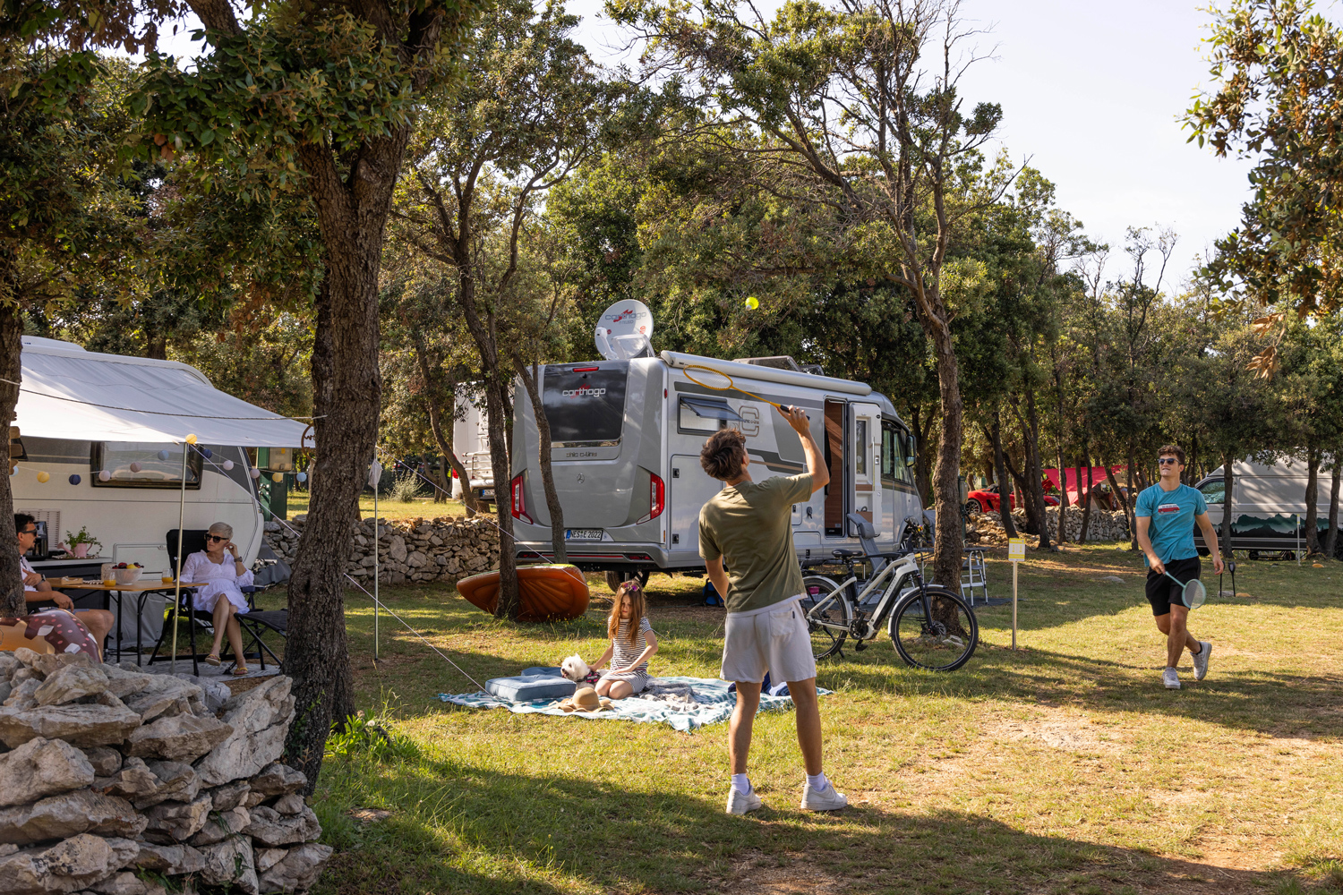spielende Jugendliche vor Wohnmobilen mit Eltern auf dem großzügigen
                                 Stellplatz im Wald