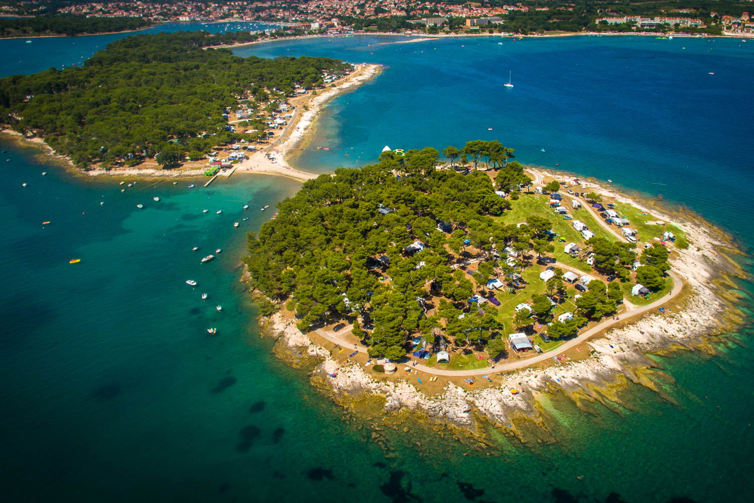 Luftbildaufnahme des Arena Medulin Campsite. Der Campingplatz liegt auf einer kleinen Insel, welche nur
                                 durch eine kleine Brücke von einer anderen Halbinsel aus erreichbar ist. Die Insel ist stark bewaldet und die Plätze sind
                                 stark besetzt.