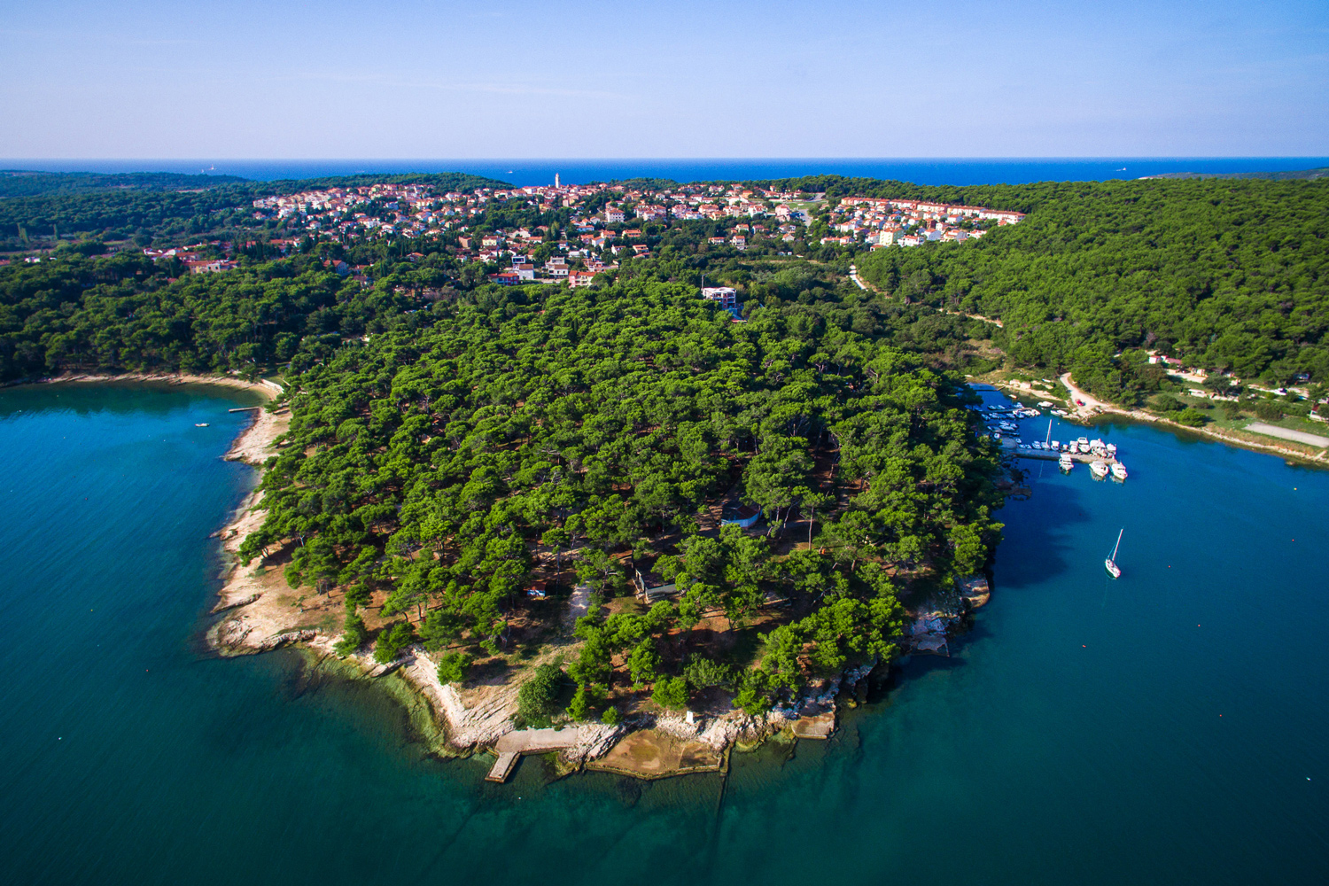 Luftbildaufnahme des Arena Runke Campsite. Der Campingplatz liegt
                                 direkt am Wasser, dicht bewaldet, in der Nähe einer kleinen Stadt in Kroatien. Beim Campingplatz ist zudem ein kleiner Hafen,
                                 an dem einige Boote stehen.