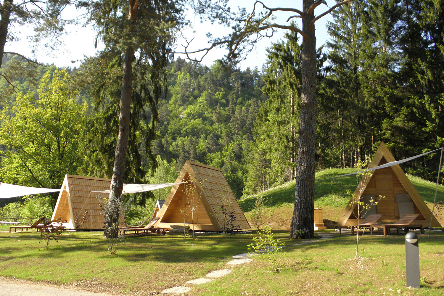 Auf dem Bild zu sehen sind dreieckige Holzhütten/Unterkünfte im bewaldeten Sava Camping Bled.
