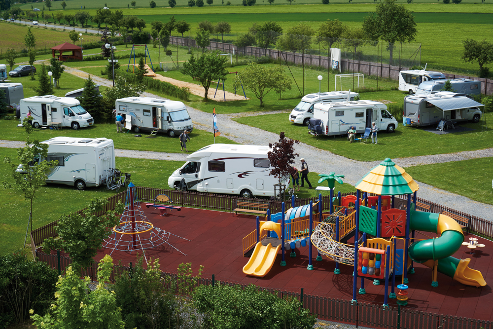 Belegte
Stellplätze der Camping Oase Praha mit Kinderspielplatz im Vordergrund und Fußballplatz und Wiesen im Hintergrund.