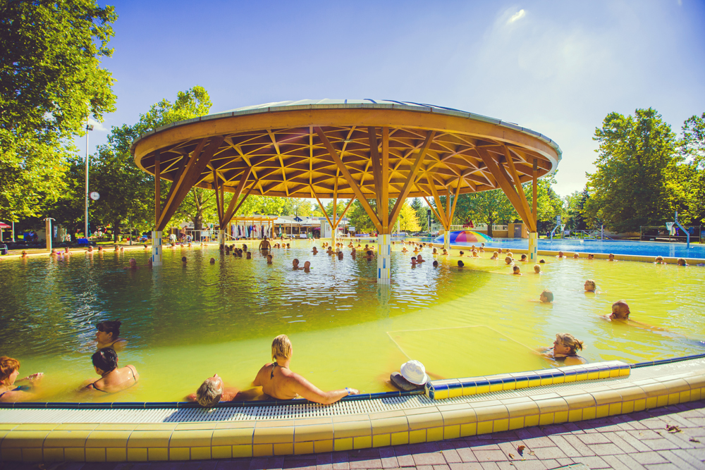 Außenpool/Schwimmbereich des Thermal Camping Bad Bükfürdö in Ungarn. Auf
                                 dem Bild ist ein Becken mit überdachtem Holz in der Mitte zu sehen.