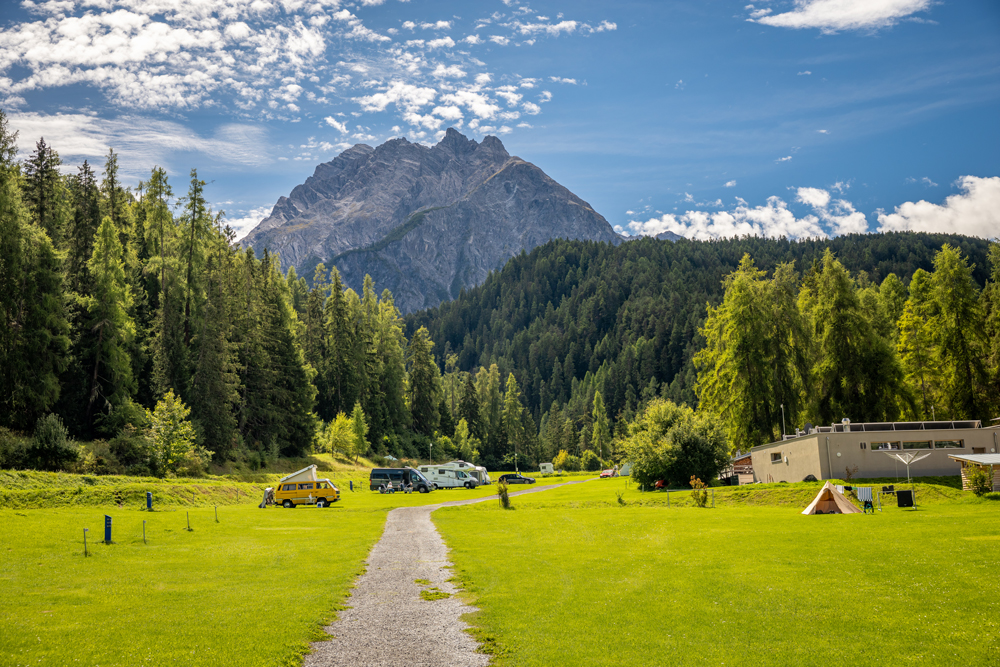 Teils belegte Wiesen-Stellplätze des TCS Camping in Scuol mit wunderschönem
Wald- und Bergpanorama im Hintergrund.