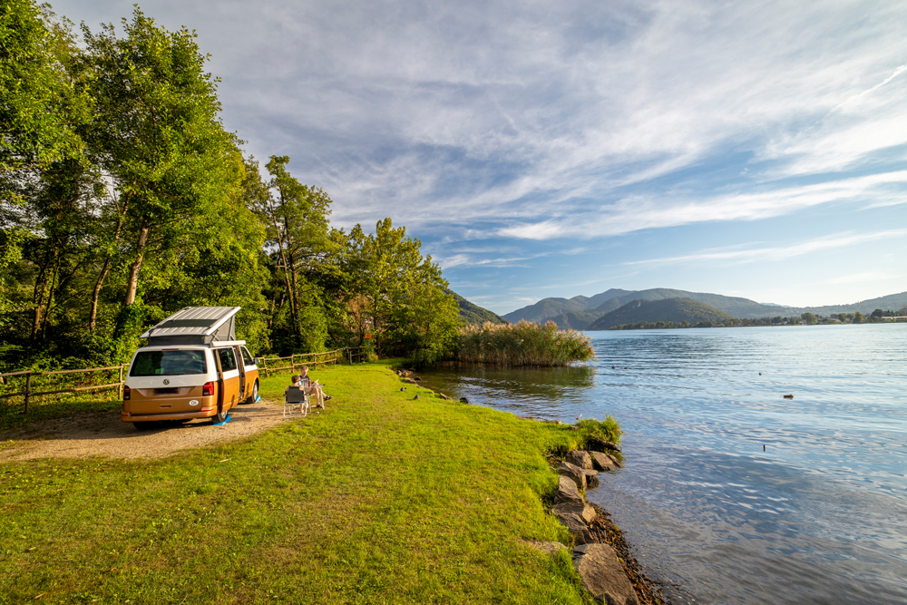 Zwei Leute auf Campingstühlen vor Van direkt
am See an einer VIP Parzelle des TCS Camping Lugano Muzzano.