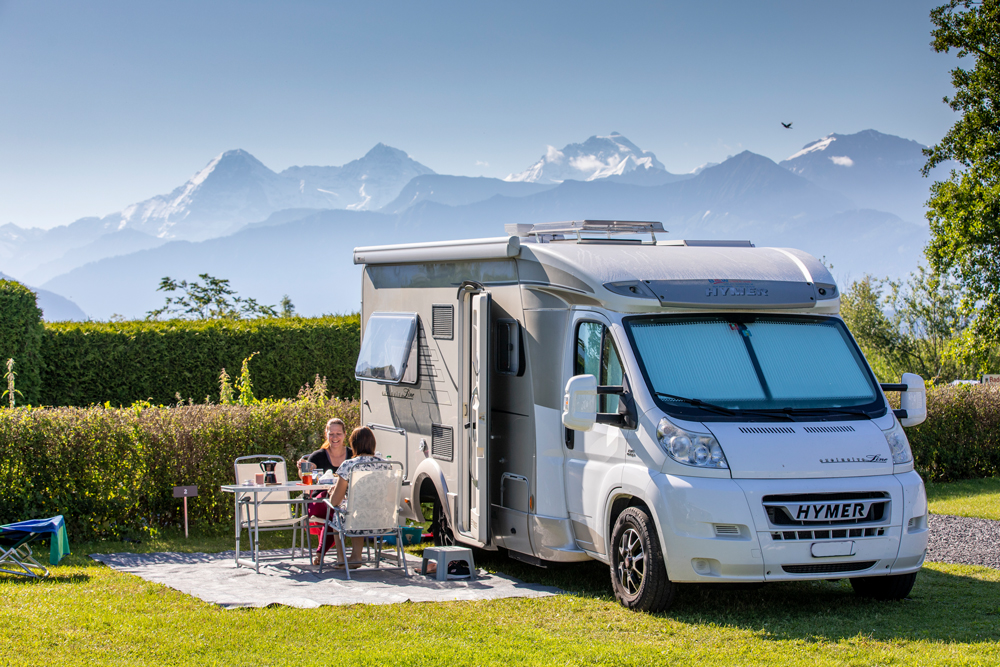 Zwei Frauen auf Campingstühlen
beim Tisch vor einem Wohnmobil auf dem TCS Camping Gwatt Thunersee mit Bergpanorama im Hintergrund.