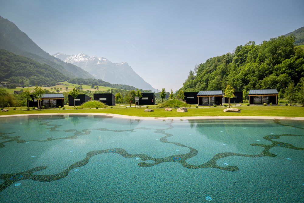 Natürlicher
Schwimmteich mit Unterkünften und Bergpanorama im Hintergrund beim TCS Camping Olivone in der Schweiz.