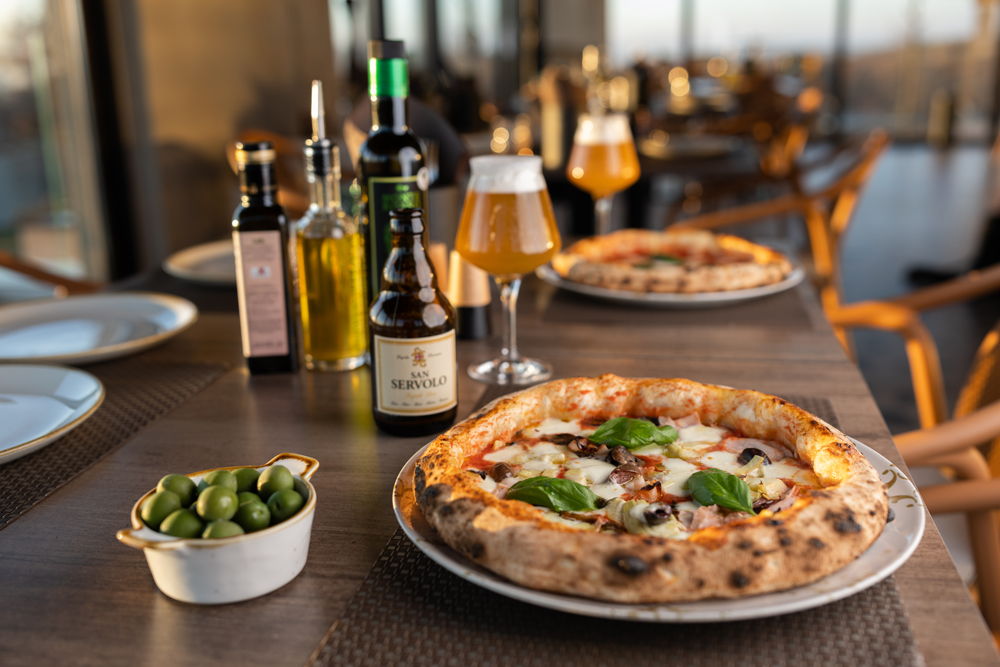 Tisch in der Pizzeria auf dem Resort San Servolo gedeckt mit Pizzen, Öl, Oliven und Bier.
