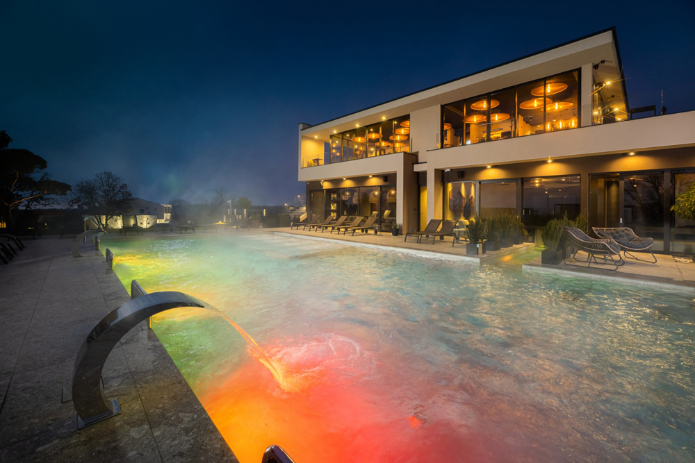 Auf dem
Bild ist ein beheizter und beleuchteter Außenpool vor einem Haus bei Nacht auf dem Resort San Servolo abfotografiert.