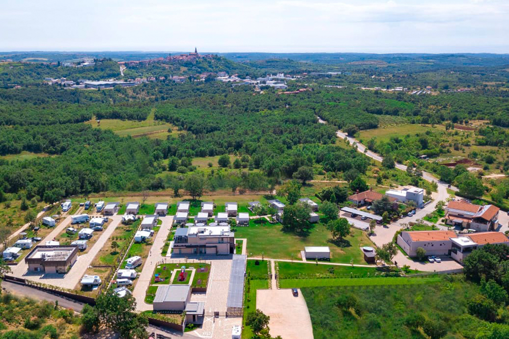 Luftbildaufnahme des Camping & Wellness Resorts San Servolo in Kroatien. Man sieht die Anlage mit Stellplätzen,
Einfahrt, usw., den dahinter liegenden Wald sowie im Hintergrund die naheliegende Stadt Buje.