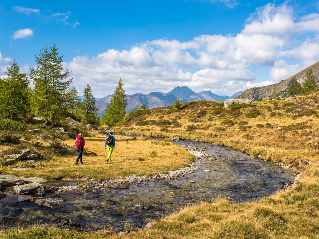 Zwei Menschen auf dem Berg beim Wandern neben einem Bach.